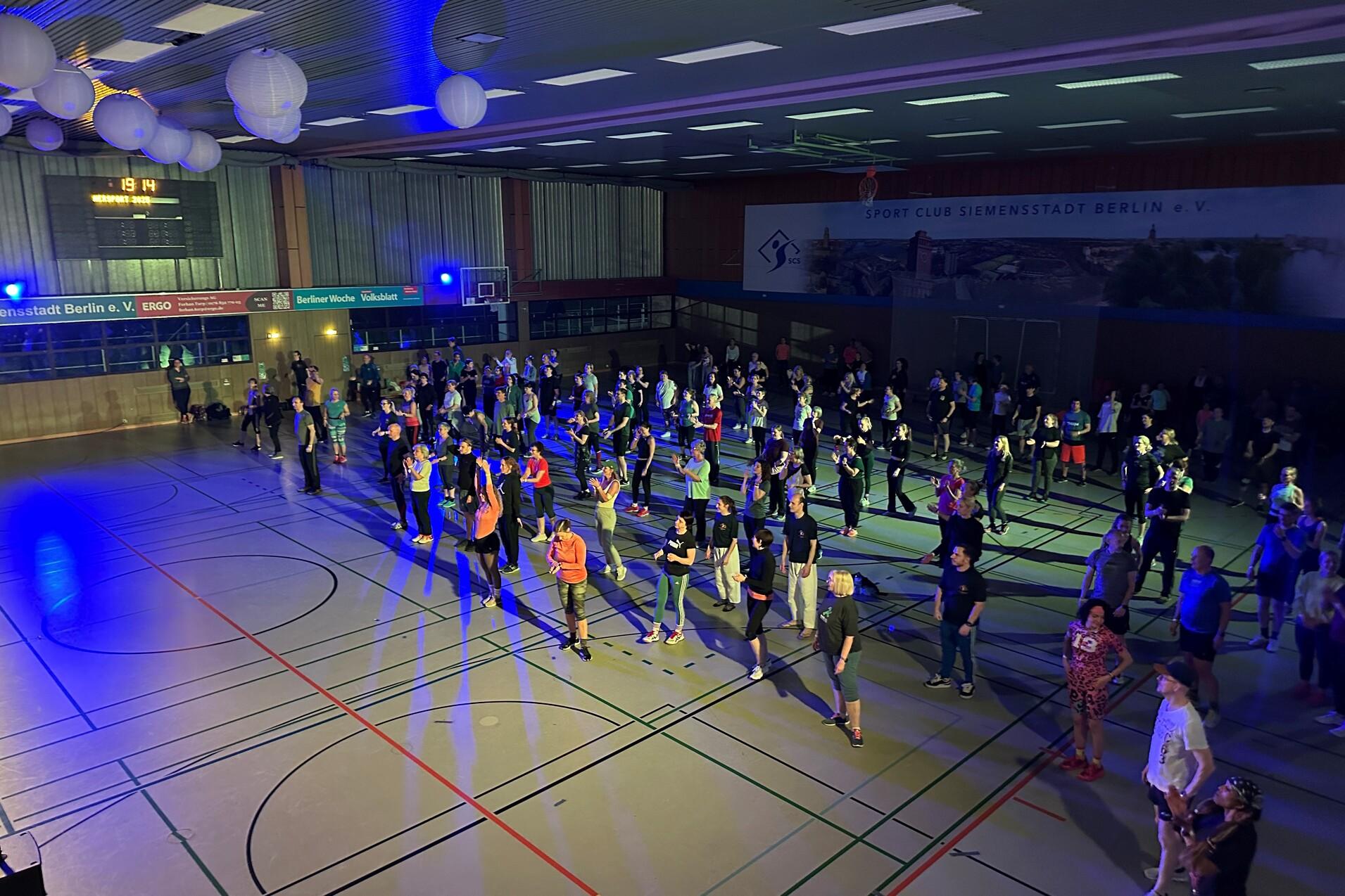 Menschen tanzen in einem hell beleuchteten Sporthall mit bunten Lichtern und dekorativen Laternen.