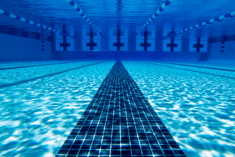 Blick auf den Swimmingpoolboden mit klar blauem Wasser und schwarzen Fliesenlinien im Schwimmbecken.