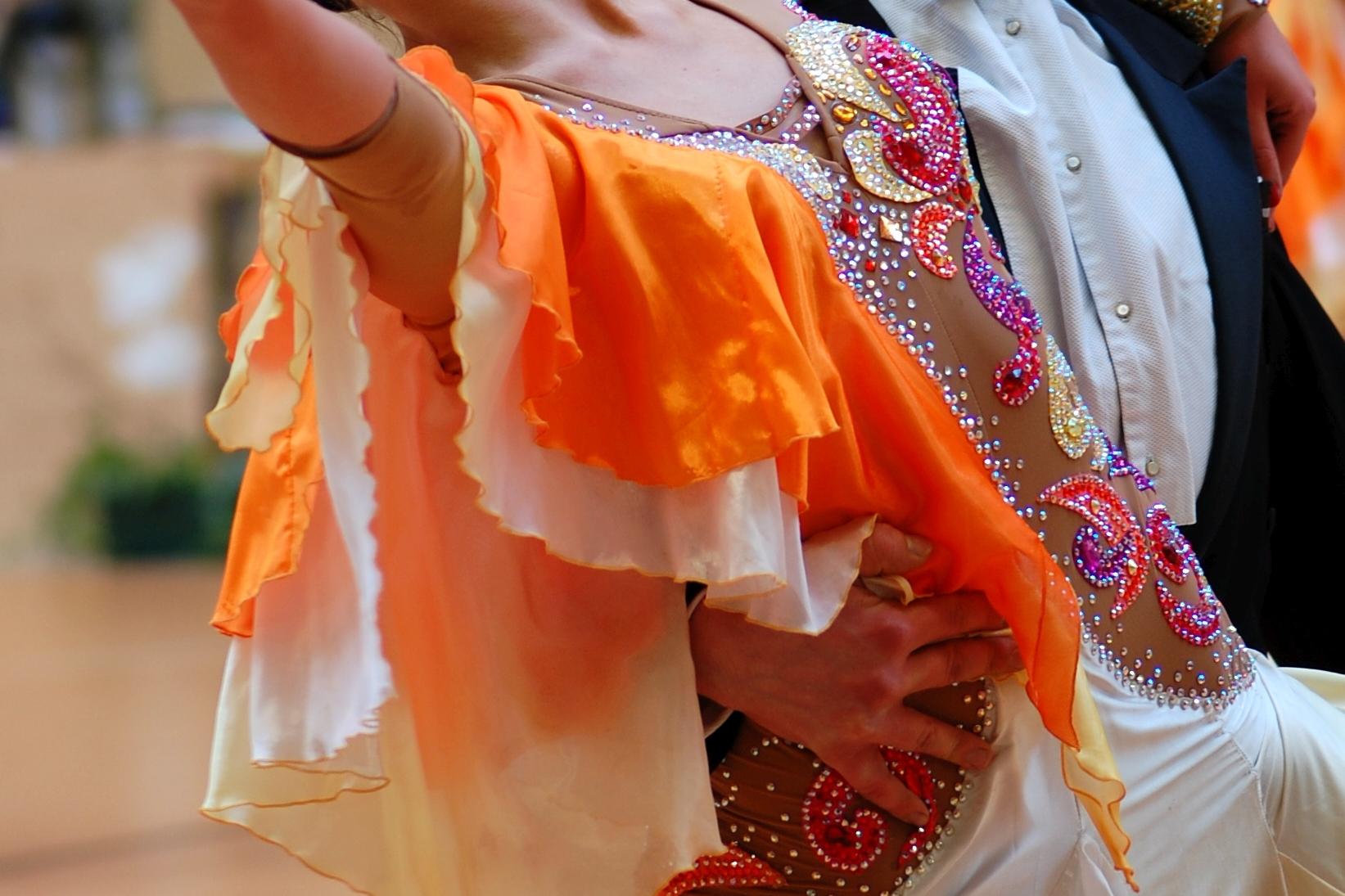 Tanzpaar in eleganter Kleidung zeigt einen Ausdruckstanz, die Frau in orange-wei&szlig;er Robe, der Mann im Smoking.