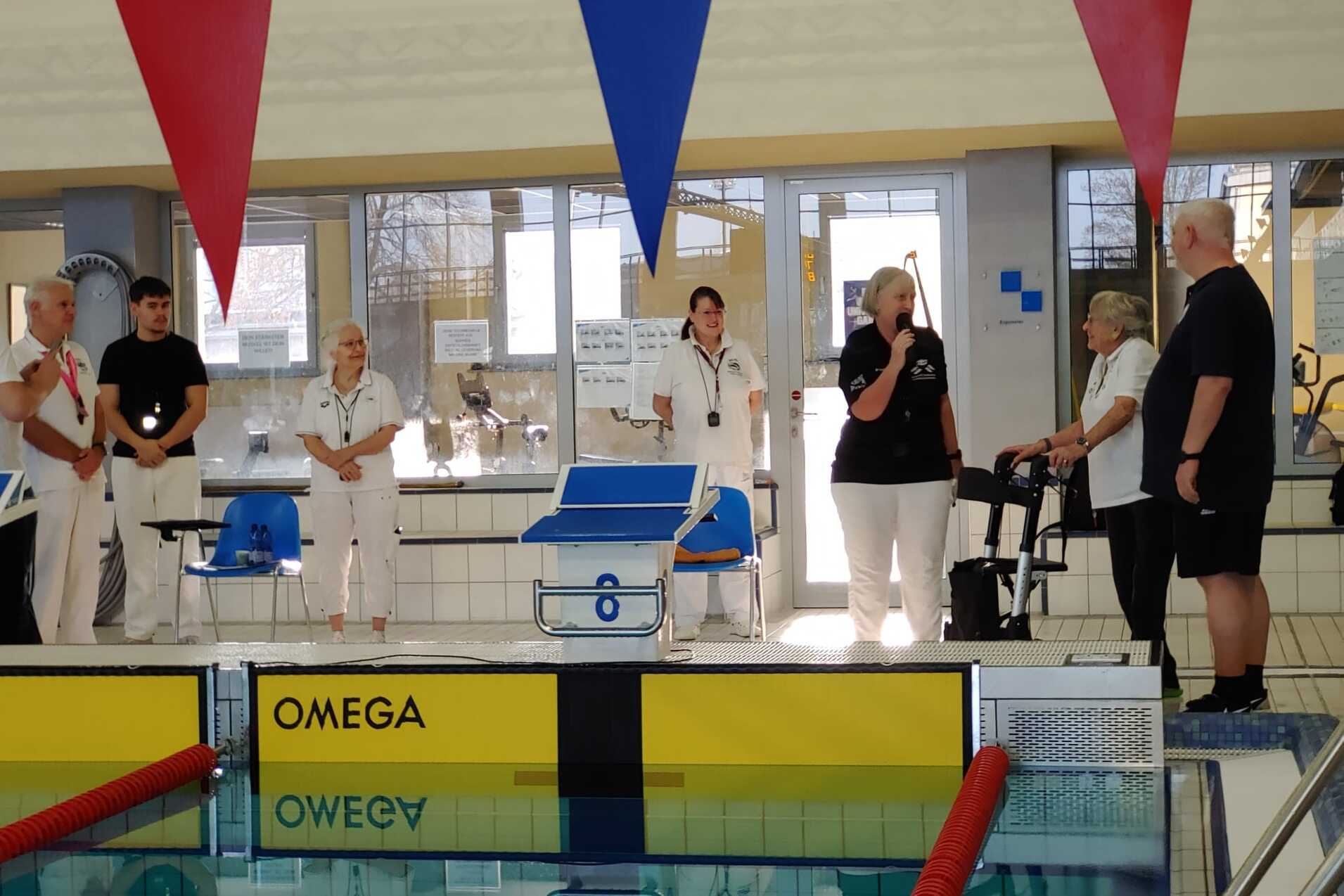 Versammlung am Schwimmbecken mit Teilnehmern in wei&szlig;er und schwarzer Kleidung, die miteinander sprechen und zuh&ouml;ren.