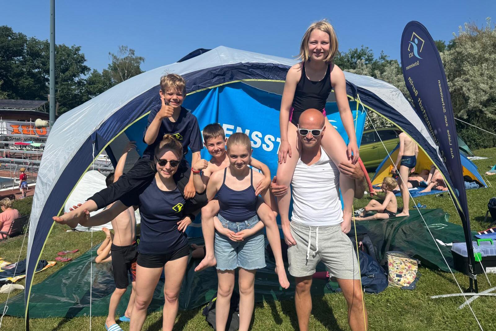Gruppe von sechs Personen posiert unter einem Zelt bei sonnigem Wetter in einem Freibad.