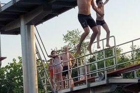 Gruppenspringer auf einem Sprungbrett, w&auml;hrend andere Schwimmer am Beckenrand warten. Sommerliche Atmosph&auml;re im Freibad.