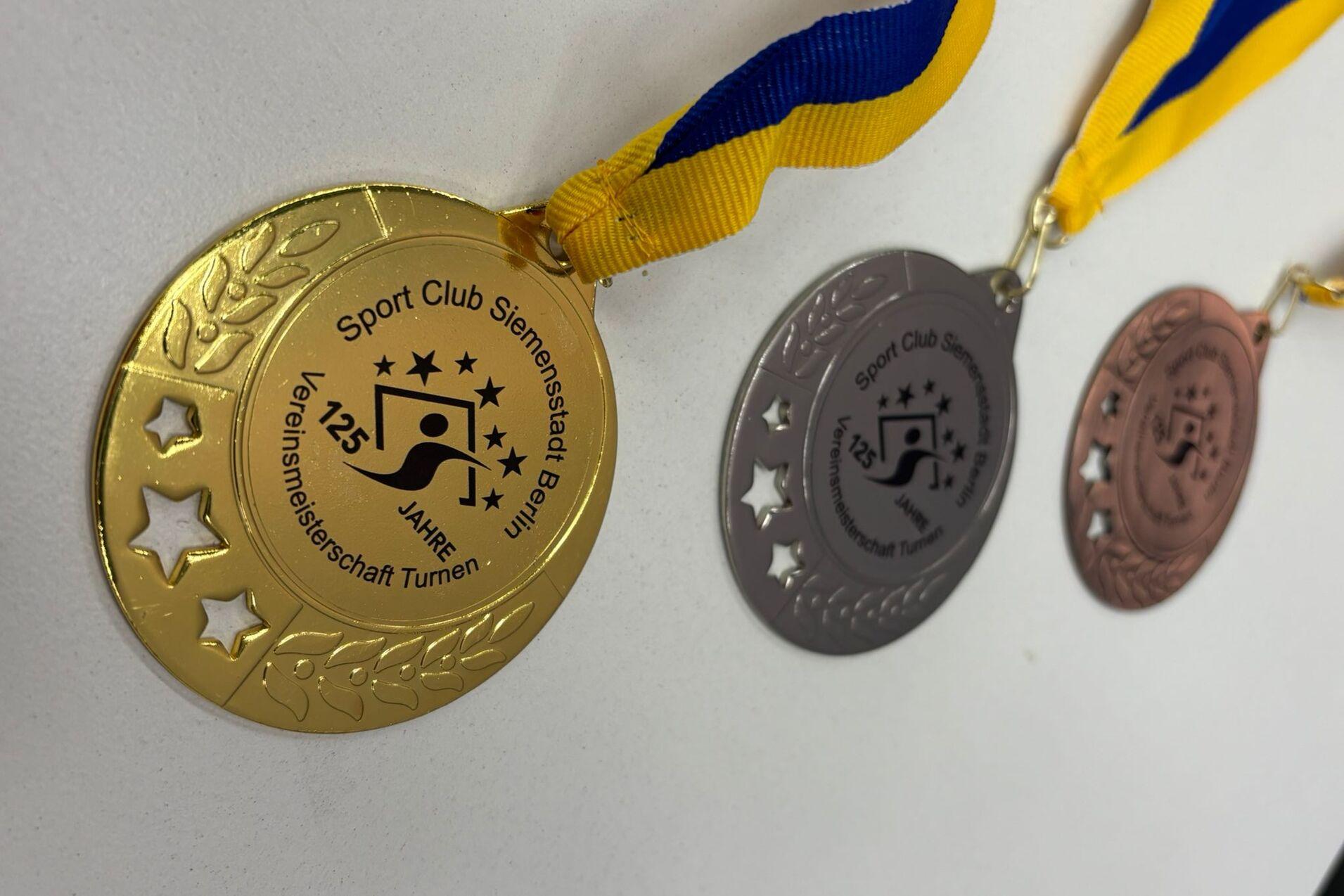 Drei Medaillen in Gold, Silber und Bronze mit gelb-blauen B&auml;ndern des Sport Clubs Siemensstadt zum 125-j&auml;hrigen Bestehen.