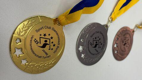 Drei Medaillen in Gold, Silber und Bronze mit gelb-blauen Bändern des Sport Clubs Siemensstadt zum 125-jährigen Bestehen.