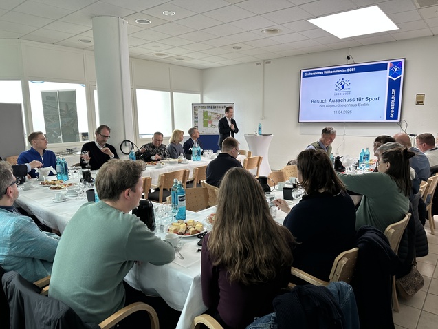 Gruppentreffen im SCSI mit Anwesenden am Tisch, Präsentation im Hintergrund, Speisen und Getränke auf dem Tisch.