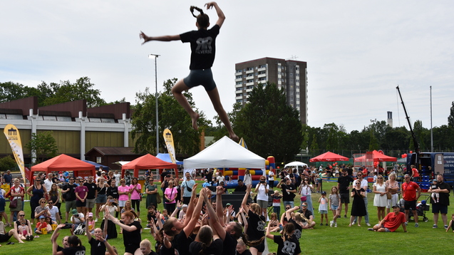 Sprung einer T&auml;nzerin von einer Menschentraube auf einer Freiluftveranstaltung mit Zuschauern.