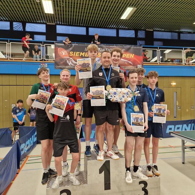 Siegerehrung mit mehreren Jugendlichen auf dem Treppchen, die Medaillen und Urkunden in einer Sporthalle halten.