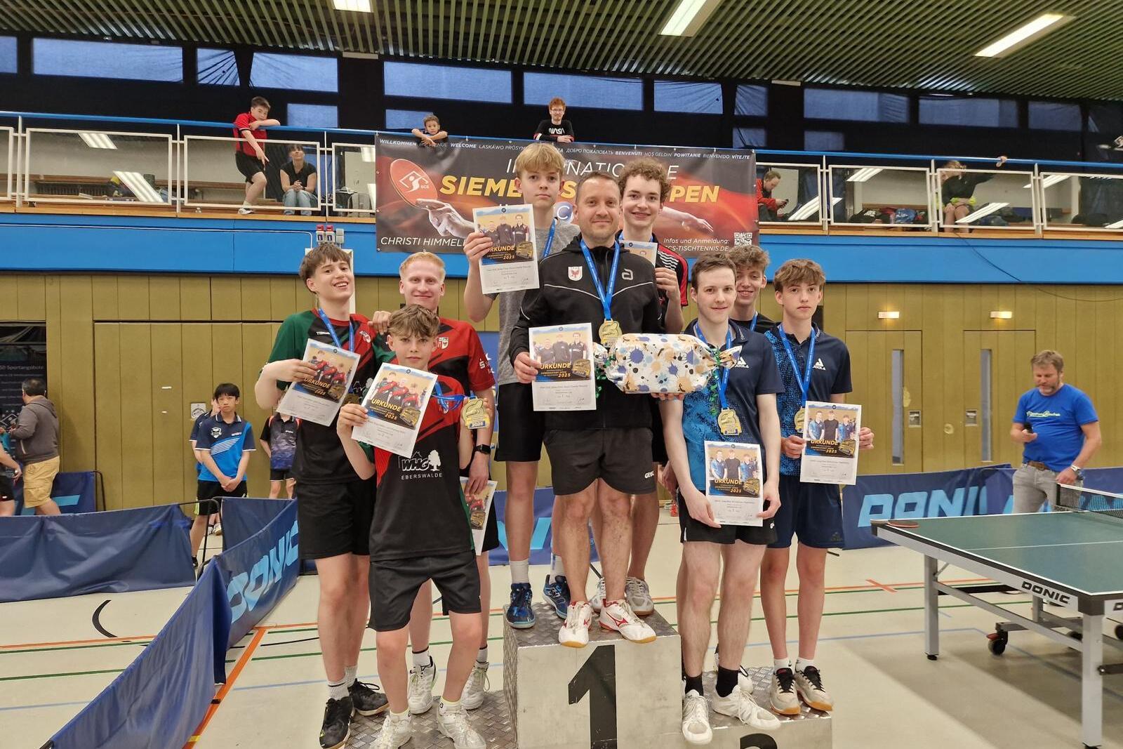 Siegerehrung mit mehreren Jugendlichen auf dem Treppchen, die Medaillen und Urkunden in einer Sporthalle halten.