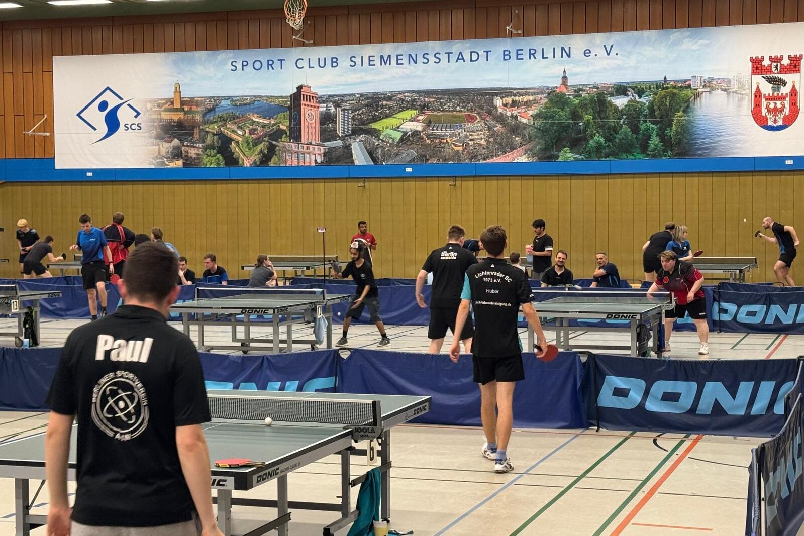 Tischtennistraining mit mehreren Spielern an verschiedenen Tischen in einer Sporthalle des SC Siemensstadt in Berlin.