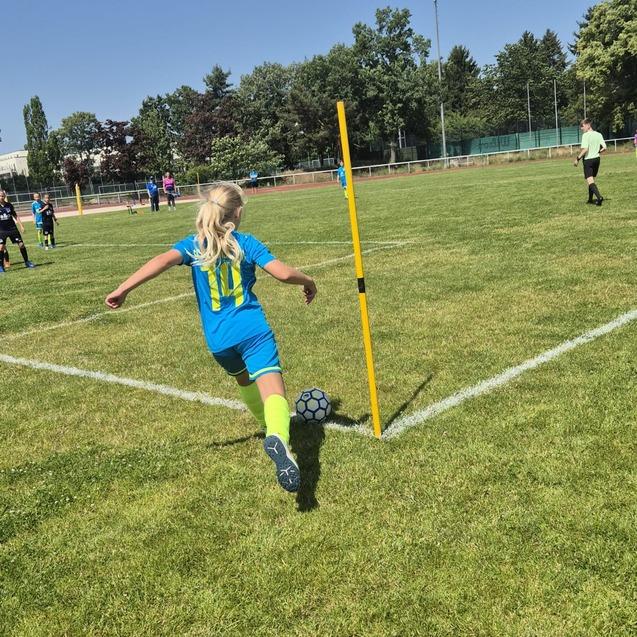 M&auml;dchen in blauer Sportbekleidung f&uuml;hrt einen Ecksto&szlig; an einem Fu&szlig;ballplatz mit gelbem Eckfahne aus.