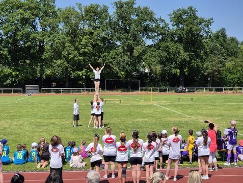 Mädchen in sportlicher Kleidung beim Cheerleading, ein Team hebt eine Person in die Höhe auf einem Sportplatz.