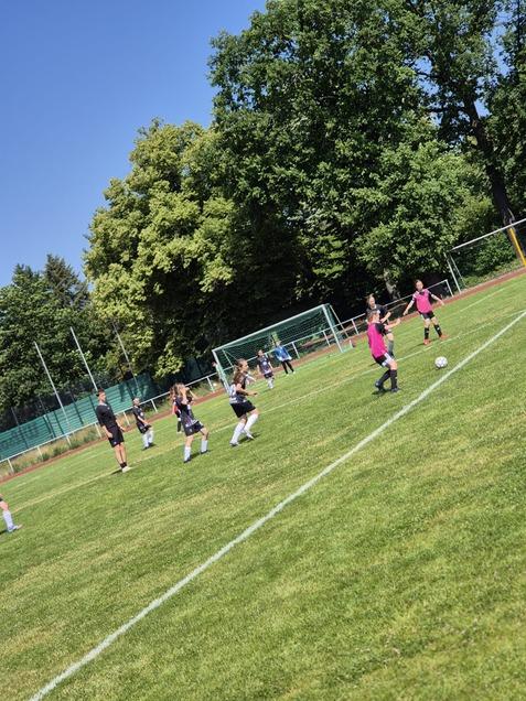 Mädchen beim Fußballtraining auf einem grünen Platz, umgeben von Bäumen und einem klaren Himmel.