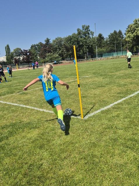 Mädchen in blauer Sportbekleidung führt einen Eckstoß an einem Fußballplatz mit gelbem Eckfahne aus.
