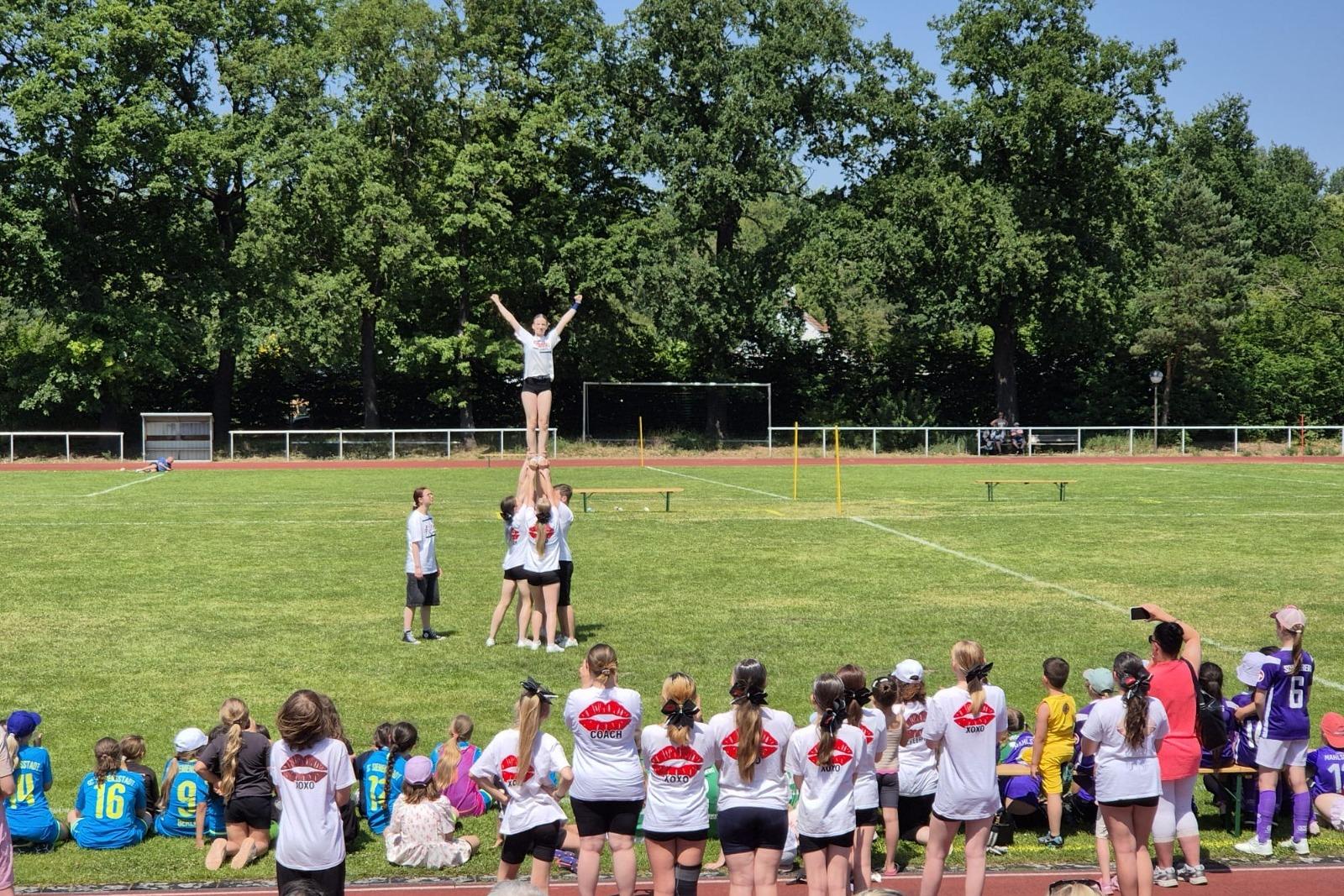 M&auml;dchen in sportlicher Kleidung beim Cheerleading, ein Team hebt eine Person in die H&ouml;he auf einem Sportplatz.