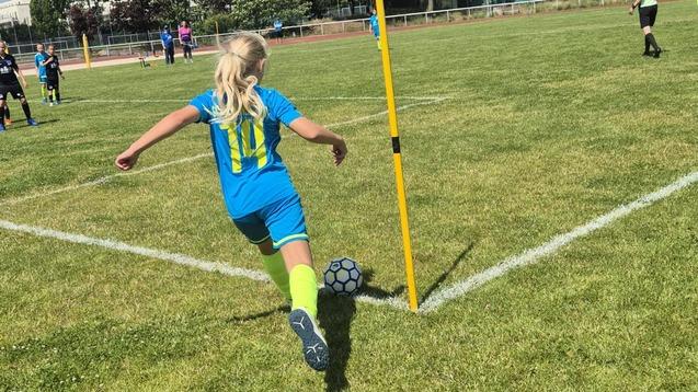 Mädchen in blauer Sportbekleidung führt einen Eckstoß an einem Fußballplatz mit gelbem Eckfahne aus.