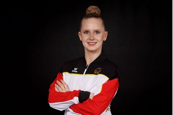 Porträt einer sportlichen Frau mit einem bunten Trainingsanzug, die in die Kamera lächelt und gekreuzte Arme hat.