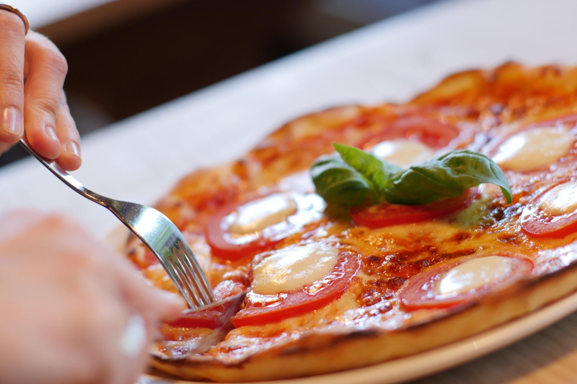 Eine Person schneidet eine Pizza mit Tomaten, Mozzarella und Basilikum auf einem Teller.