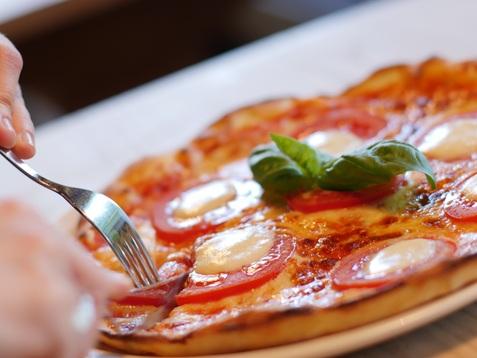 Eine Person schneidet eine Pizza mit Tomaten, Mozzarella und Basilikum auf einem Teller.