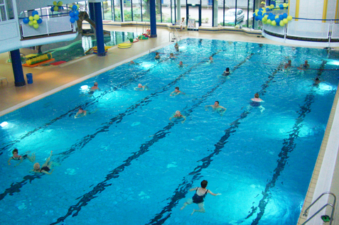 Schwimmbecken mit schwimmenden Personen und blauen und gelben Luftballons an der Decke in einem Innenbereich.