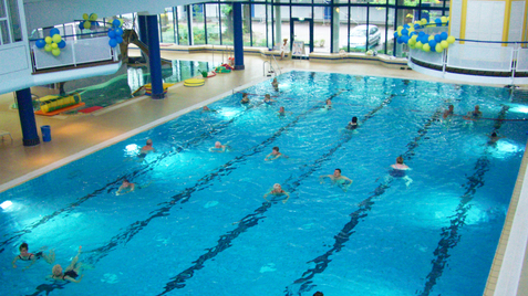 Schwimmbecken mit schwimmenden Personen und blauen und gelben Luftballons an der Decke in einem Innenbereich.