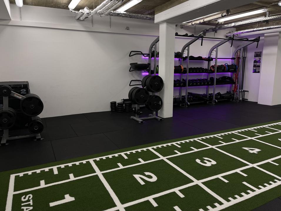 Modernes Fitnessstudio mit Gewichten und Trainingsger&auml;ten auf schwarzem Boden, gr&uuml;nem Sportteppich mit Nummern.