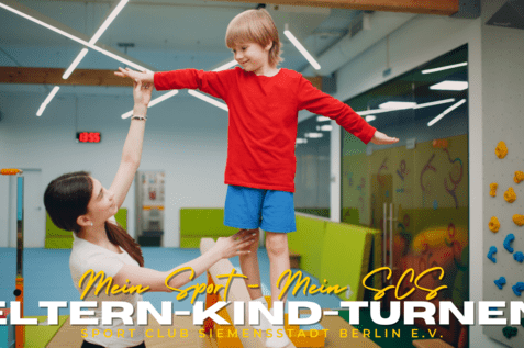 Mutter hebt lächelnd ihren Sohn in rotem Shirt während des Eltern-Kind-Turnens in einem Sportclub.