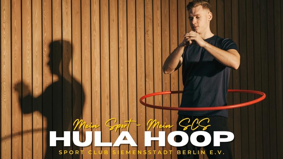 Mann mit Hula-Hoop-Reifen vor einer Holzlattenwand, konzentriert und in Bewegung.