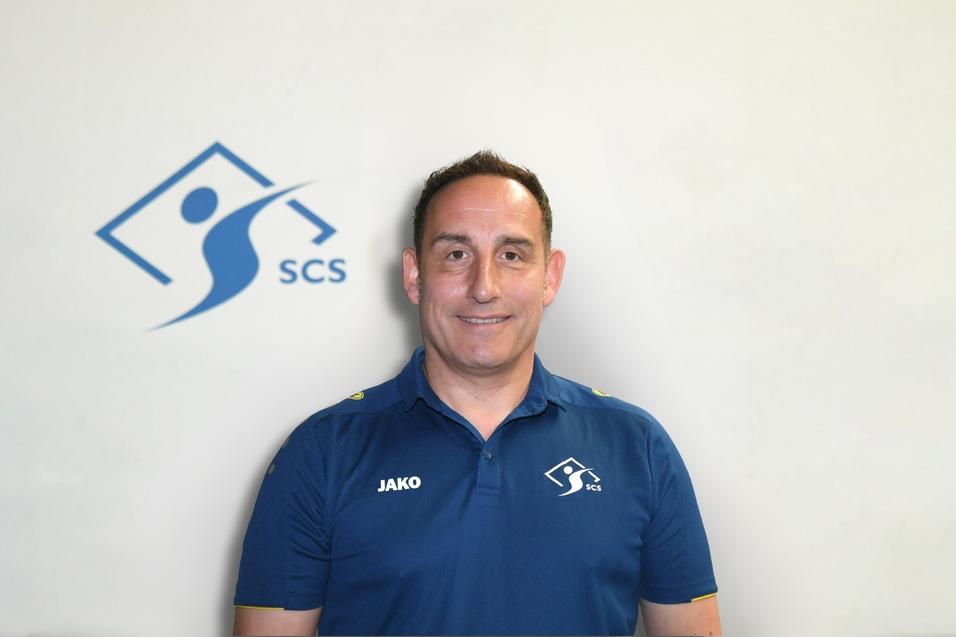 Porträt eines Mannes in einem blauen Polo mit dem Schriftzug "JAKO" vor einem hellen Hintergrund mit dem SCS-Logo.