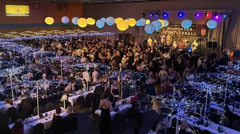 Große Veranstaltungshalle mit festlich geschmückten Tischen, Tänzern und einer Band auf der Bühne beim Spandauer Sportlerball.