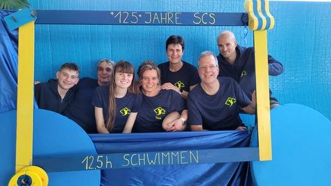 Gruppe von sechs Personen in einheitlichen T-Shirts, feiernd hinter einem Rahmen mit der Aufschrift „125 Jahre SCS“.