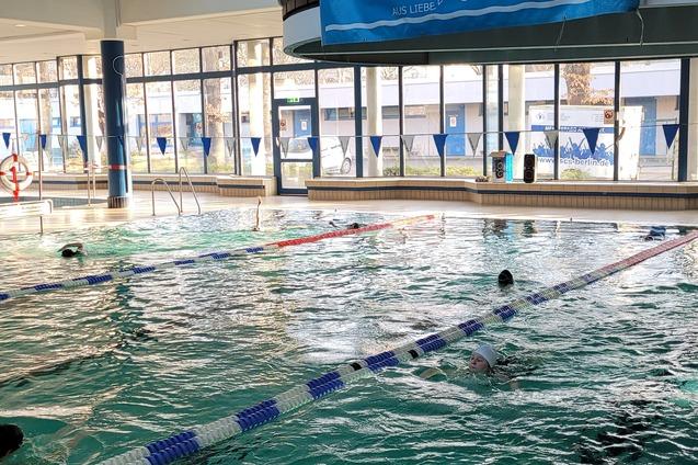 Blick auf ein Schwimmbad mit Schwimmern im Wasser und einem Banner des SC Siemensstadt Berlin im Hintergrund.