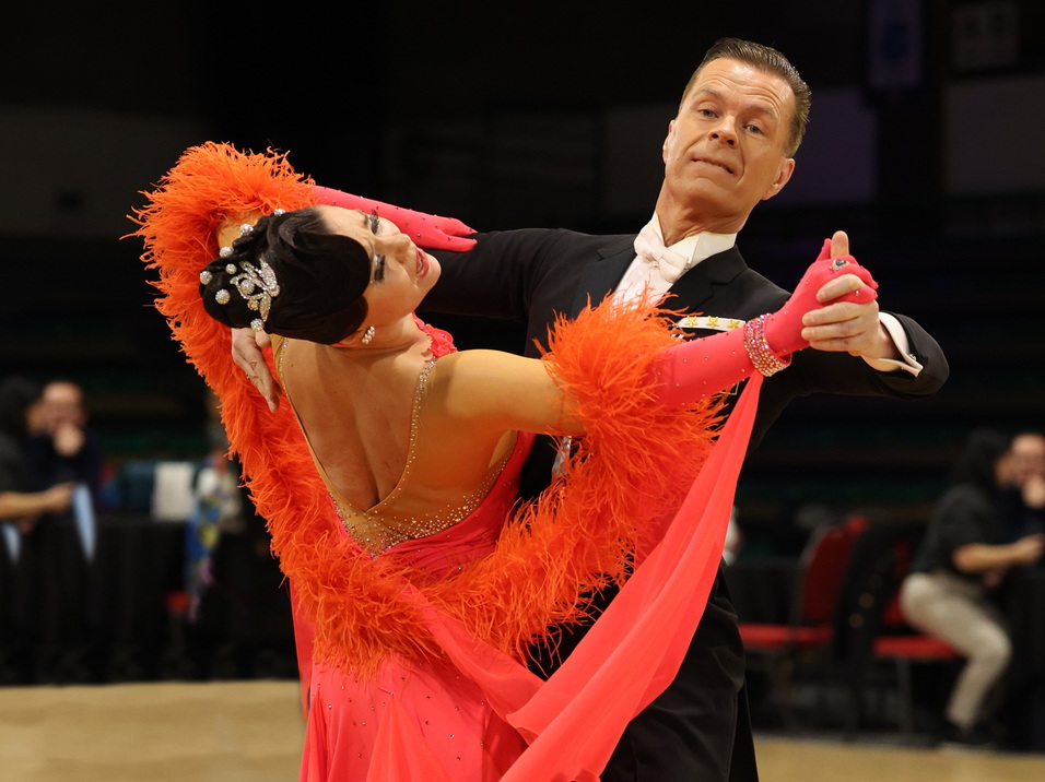 Tanzpaar in eleganter Kleidung, leidenschaftlich tanzend auf einer Turnierfläche mit Holzfußboden.