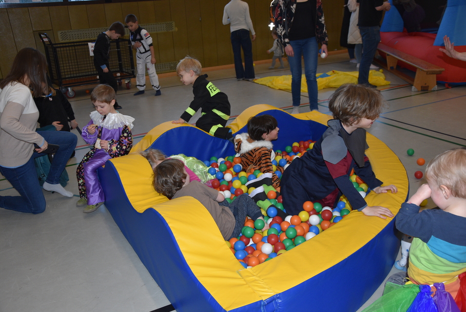 Kinder spielen in einem großen Bällebad mit bunten Kunststoffbällen in einer Turnhalle.