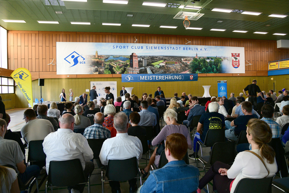 Blick auf eine versammelte Menge während einer Veranstaltung im Sport Club Siemensstadt mit Auszeichnungen im Hintergrund.