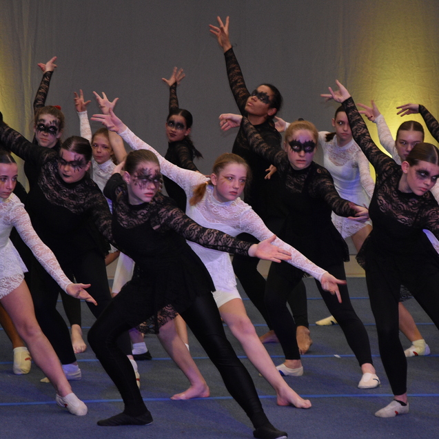 Gruppe junger T&auml;nzerinnen in schwarz-wei&szlig;en Kost&uuml;men mit Schminke, die synchron eine Tanzpose auf einer B&uuml;hne einnehmen.