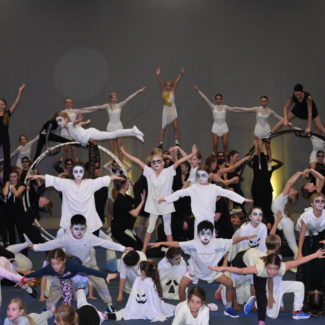 Gro&szlig;e Gruppe von Kindern in Kost&uuml;men mit Schminke, die akrobatische Figuren auf einer B&uuml;hne ein&uuml;ben.