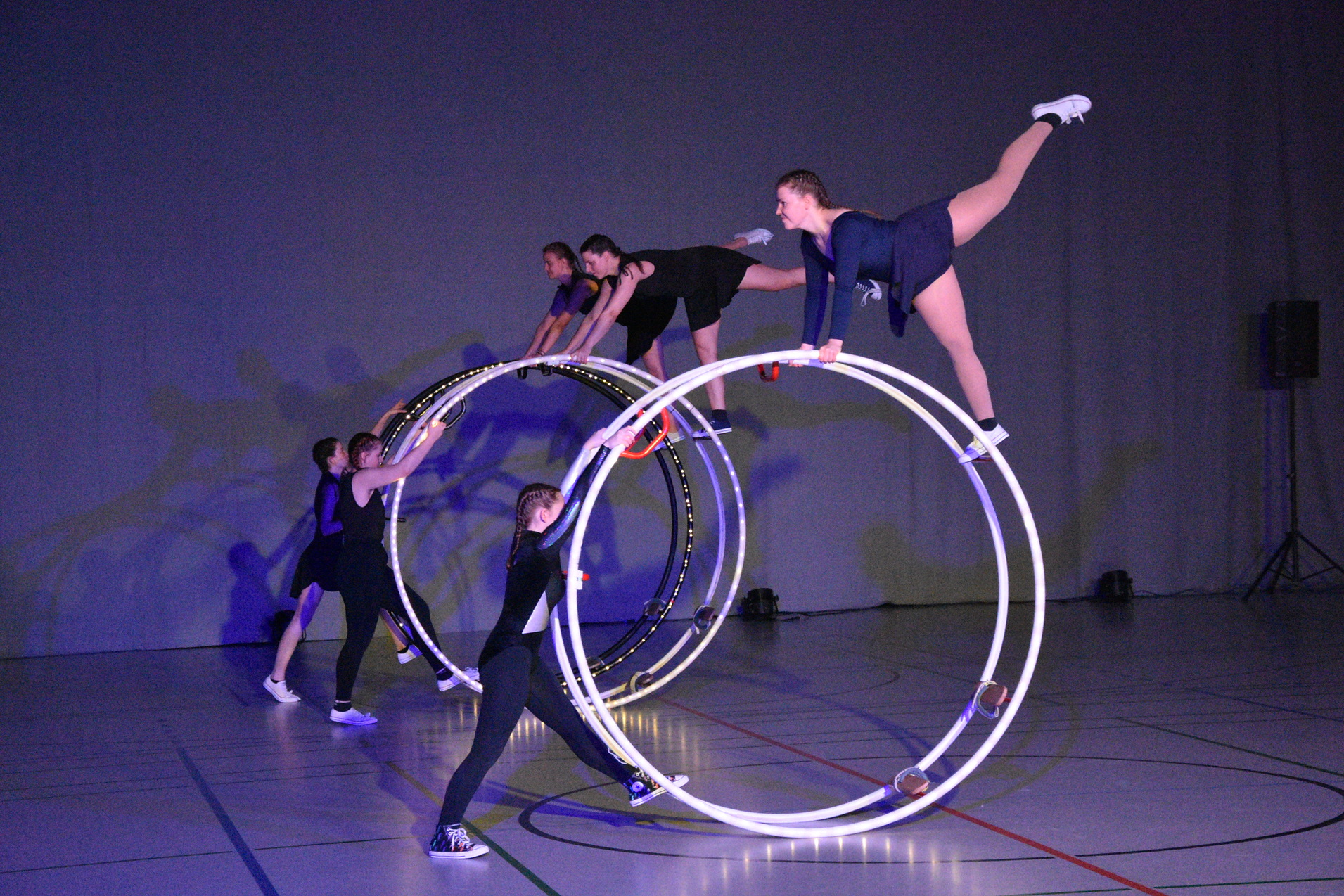F&uuml;nf Akrobatinnen stehen auf drei gro&szlig;en Zirkusr&auml;dern in einer Sporthalle und zeigen eine Kreativperformance.