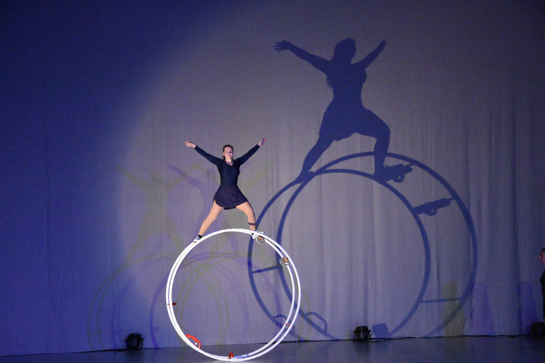 Akrobatin balanciert auf einer gro&szlig;en wei&szlig;en Requisite, w&auml;hrend Schatten an der Wand sichtbar sind.