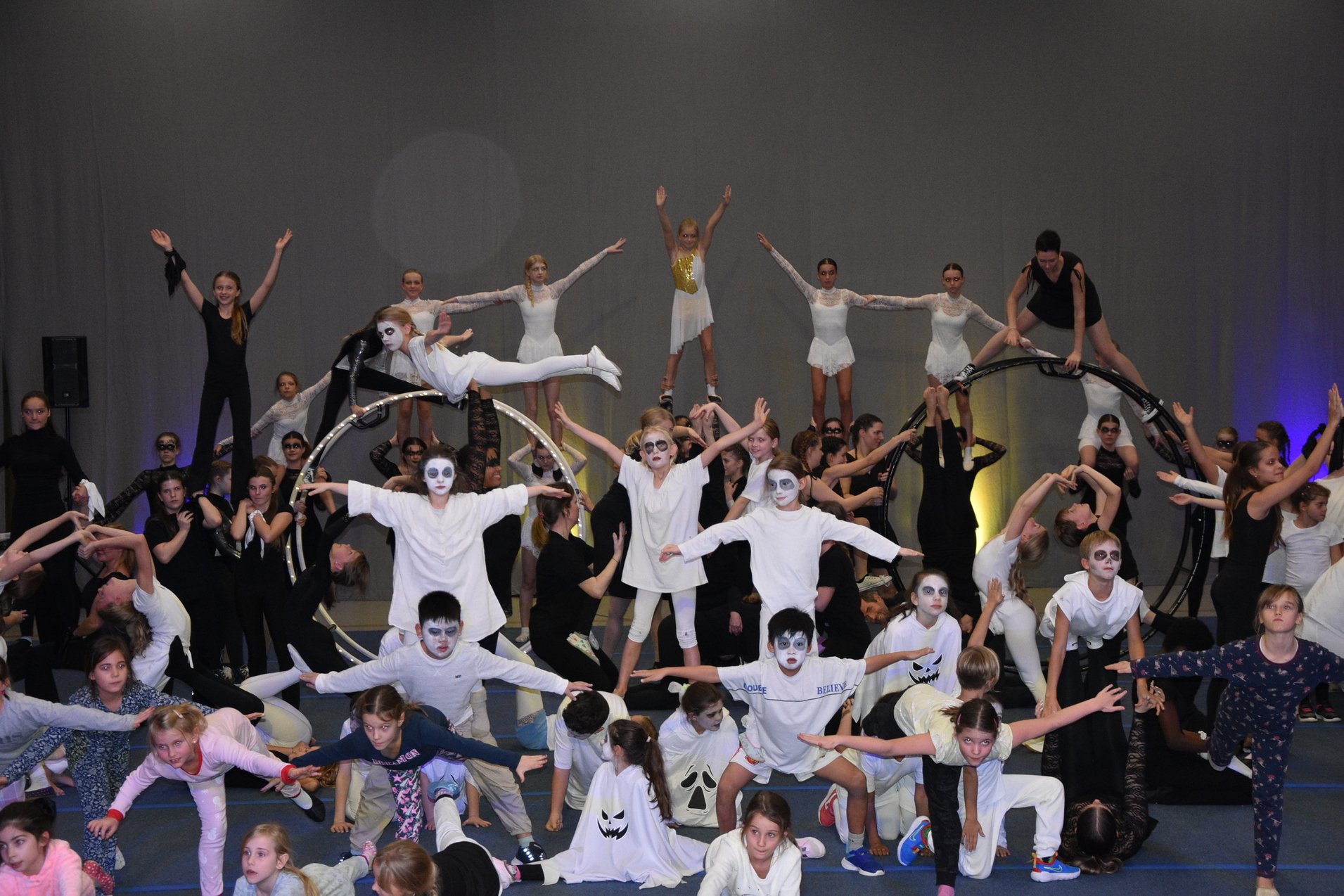 Gro&szlig;e Gruppe von Kindern in Kost&uuml;men mit Schminke, die akrobatische Figuren auf einer B&uuml;hne ein&uuml;ben.