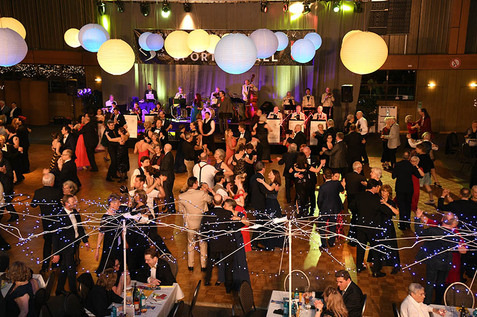 Tanzende Menschen auf einem Ball, umgeben von dekorativen Laternen und einer Live-Band im Hintergrund.