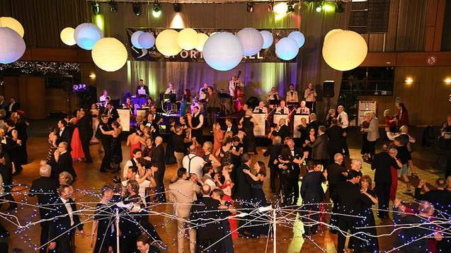 Tanzende Menschen auf einem Ball, umgeben von dekorativen Laternen und einer Live-Band im Hintergrund.