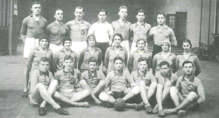Gruppenvorstellung von 15 Männern und 6 Frauen in Sportkleidung, sitzend mit einem Ball auf dem Boden, in historischer Umgebung.