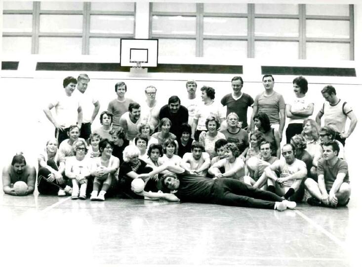 Gruppenszenen mit 40 Personen in einer Sporthalle, einige halten einen Basketball, andere sitzen am Boden.
