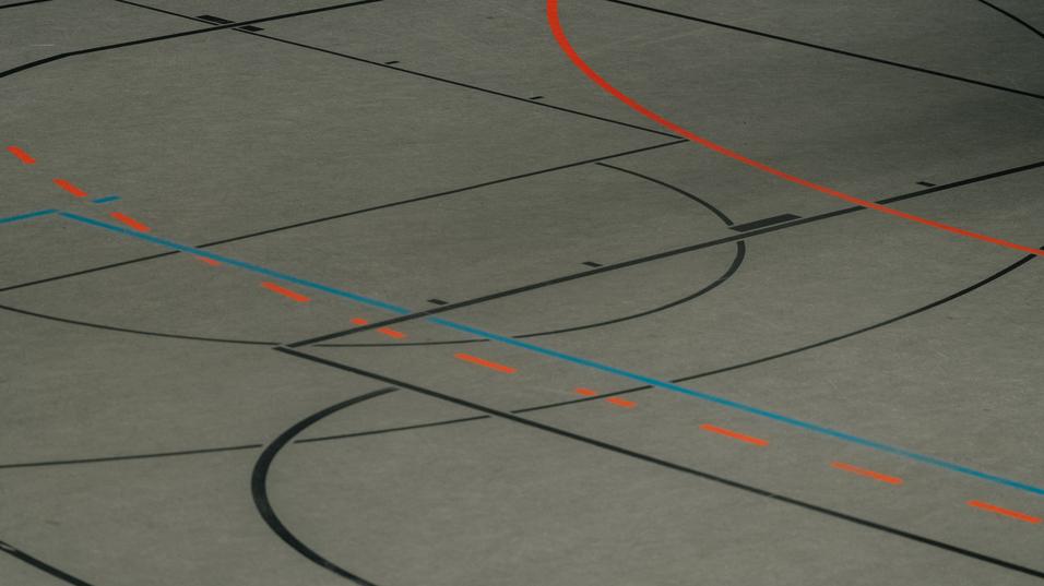 Detailaufnahme eines Sportbodens mit schwarzen, blauen und orangen Linien für verschiedene Sportarten.