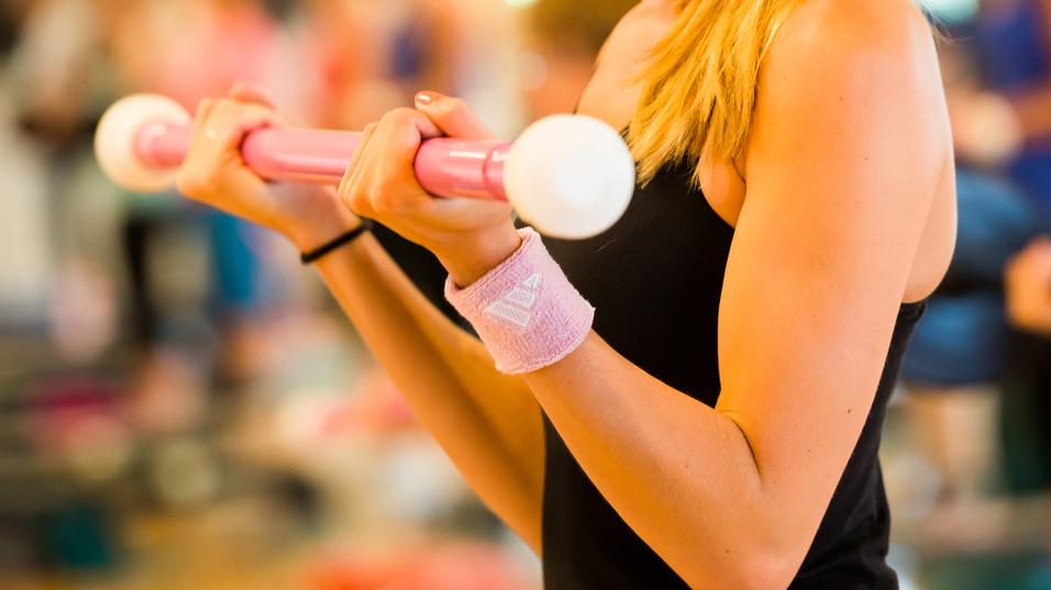 Frau hält eine pinke Hantel mit weißen Enden, während sie in einem Fitnessstudio trainiert.