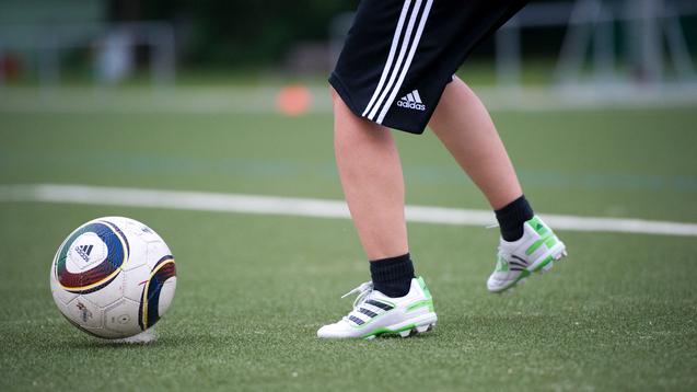 Ein Fuß mit Fußballschuhen tritt auf einen Fußball auf einem Kunstrasenfeld.