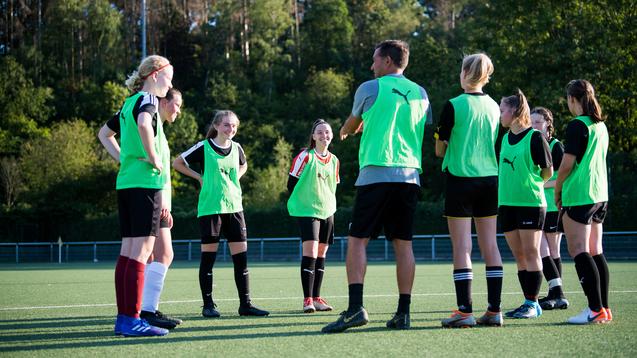 Mannschaftstraining mit Trainer: Gruppen von Mädchen tragen grüne Trainingswesten auf einem Fußballplatz.