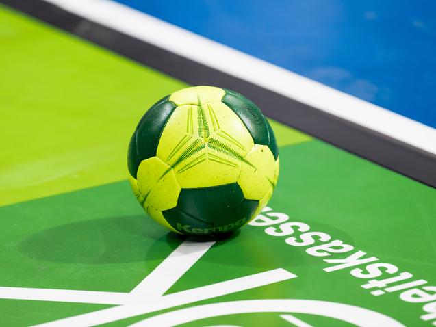 Grüner und gelber Handball liegt auf einer grünen Spielfläche mit weißem Schriftzug.