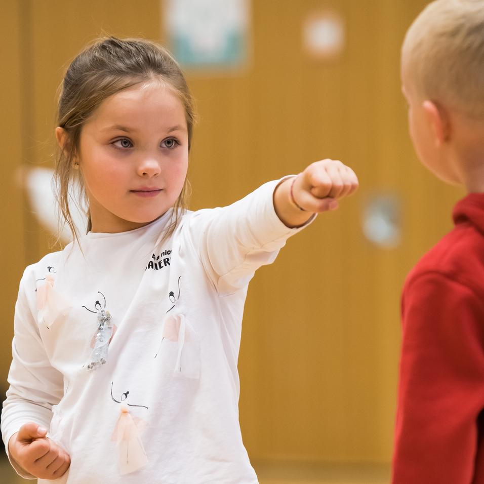 Mädchen mit gestrecktem Arm in Sportkleidung führt eine Karatebewegung im Trainingsraum aus.