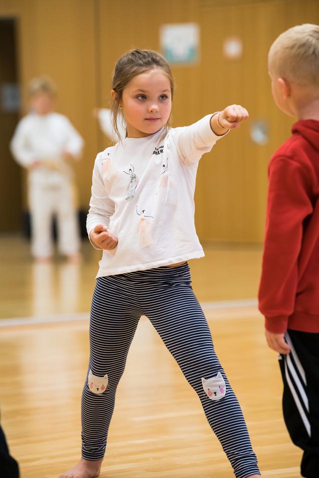 Mädchen mit gestrecktem Arm in Sportkleidung führt eine Karatebewegung im Trainingsraum aus.